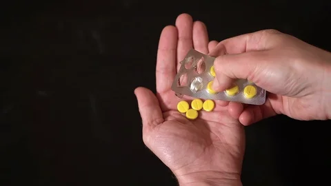 On a black background out of the blister squeezed, yellow pills in hand. Vídeos de archivo 128841034