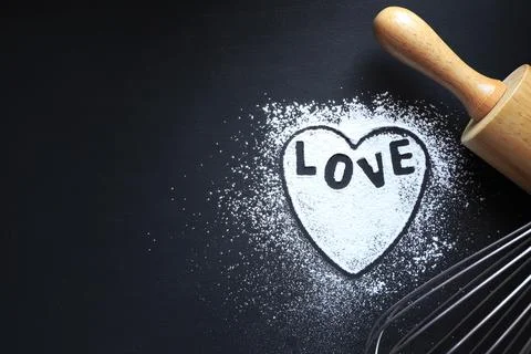 Black background with rolling pin, text love, wire whisk and heart shape Stock Photos