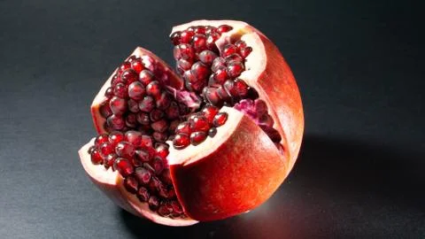 Black background, side view, in the middle of the photo an open pomegranate i Stock Photos