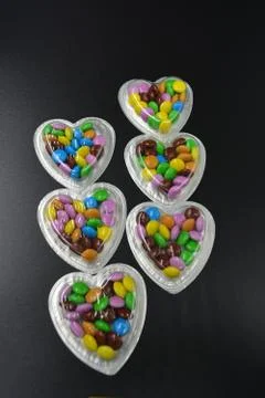 Black background with silver boxes of hearts and with multicolored chocolates Stock Photos