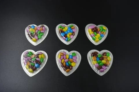 Black background with silver boxes of hearts and with multicolored chocolates Foto stock