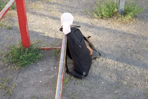 Black backpack and white cap resting on a metal bar outdoors Stock Photos