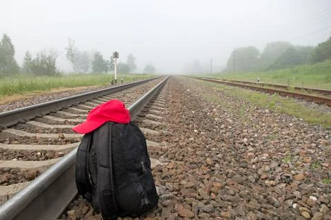 Black backpack with red baseball cap on granite shingle next to rails of railway Stock Photos