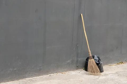 A black bag of garbage and old broom against a gray wall., with copy space fo Stock Photos