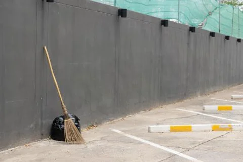A black bag of garbage and old broom against a gray wall., with copy space fo Stock Photos
