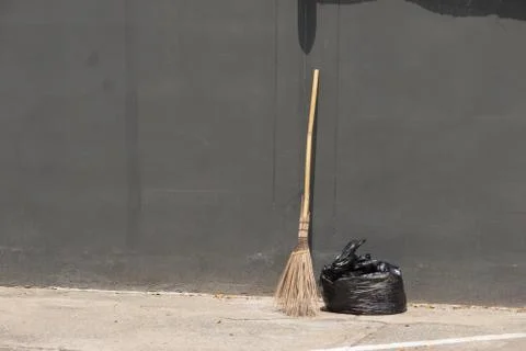 A black bag of garbage and old broom against a gray wall., with copy space fo Stock Photos