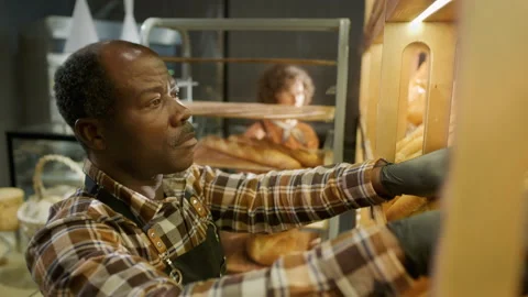 Black Bakery Worker Placing Fresh Baguettes on Bread Display for Sale Stock Footage 303459718