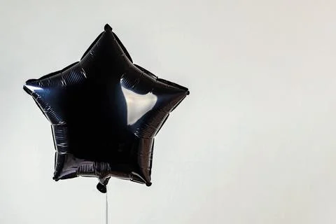 Black balloon in the shape of a star floating against a plain background, b.. Stock Photos