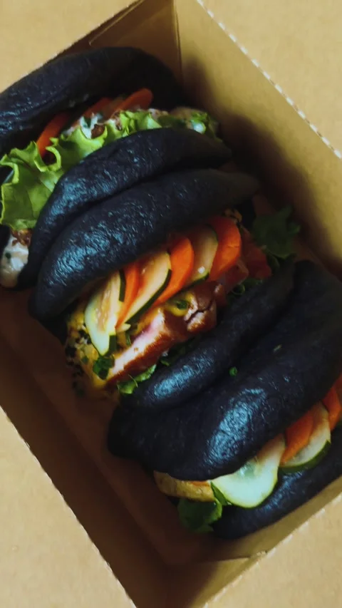 Black bao buns filled with chicken, fresh lettuce, sliced carrots, and cucumber Stock Footage 332272609