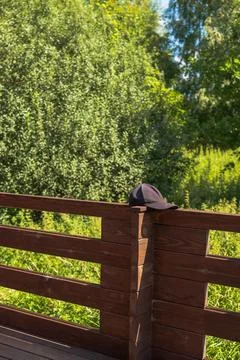 Black baseball cap on dark wooden railing in a Lithuanian park Stock Photos
