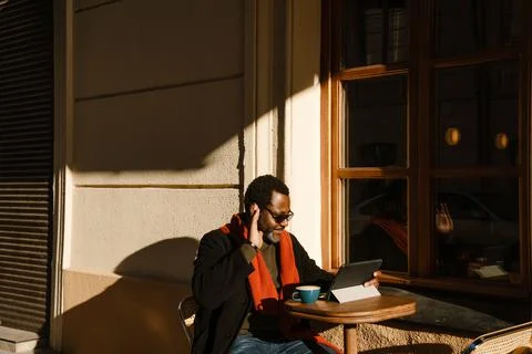 Black bearded man using tablet computer and waving hand in street cafe 写真素材