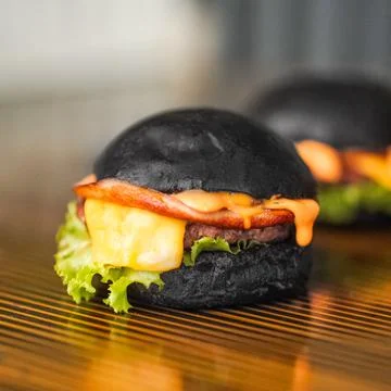 Black Beef burger filled with cheese and vegetables placed on a wooden table Stock Photos