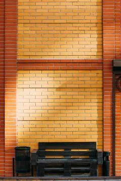 Black bench from pallets on a background of a brown brick wall with garbage c Stock Photos