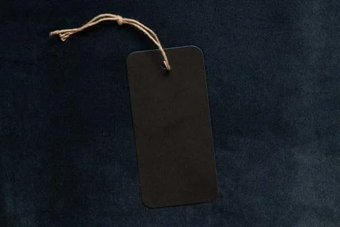 Black blank hang tag on string lies on dark blue fleecy velour fabric as mock Stock Photos