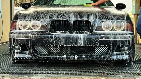 Black BMW M5 E39 covered in soap foam being hand washed with a sponge at a self Stock Footage 336718595