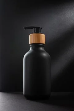 Black bottle with dispenser pump over black background. Blank product packagi Stock Photos