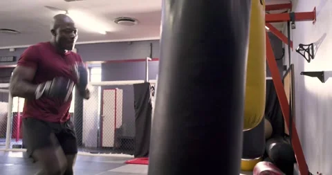 Black boxer performing footwork punching heavy bag inside boxing ring while Stock Footage 340881209