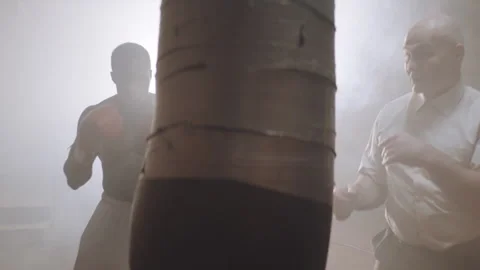 Black Boxer punching the bag a the gym while the trainer is holding it Stock Footage 282986803