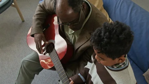 Black Boy Child Learning to Play Guitar with Granddad on Couch Stock Footage 322528280
