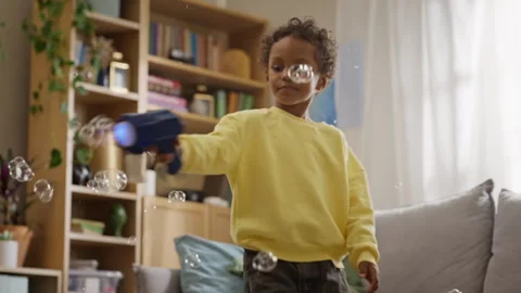 Black Boy Shooting Soap Bubbles with Toy Gun in Living Room Stock Footage 345492404