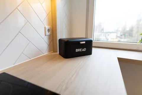 A black bread bin lying on a light wood kitchen counter. View of the city t.. Stock Photos