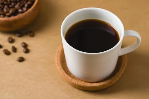 Black brewed beverage in white cup with roasted beans on warm tabletop Stock Photos