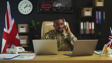 Black British soldier in headset supervises missions on laptops in military hub Stock Footage 342148879
