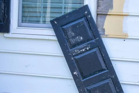 A Black Broken Window Shutter Barely Hanging Onto the Wall Stock Photos
