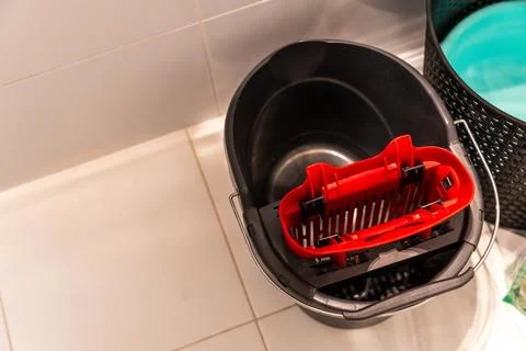 A black bucket with a red strainer placed inside, positioned on tiled floor, Stock Photos