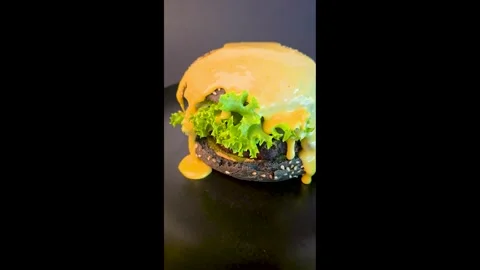 Black burger with beef patty, lettuce and sesame seed bun with cheese sauce Stock Footage 344844614