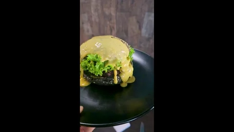Black burger with beef patty, lettuce and sesame seed bun with cheese sauce Stock Footage 344844648
