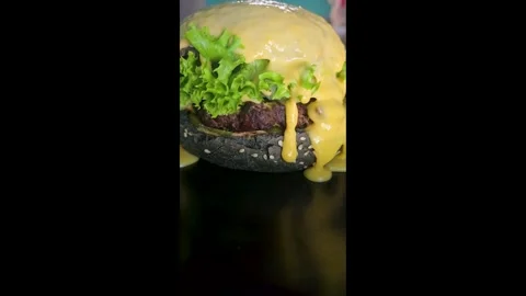 Black burger with beef patty, lettuce and sesame seed bun with cheese sauce Stock Footage 344844670