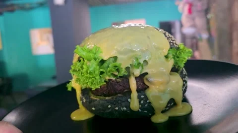 Black burger with beef patty, lettuce and sesame seed bun with cheese sauce Stock Footage 344844721