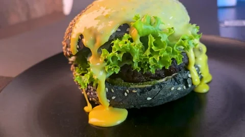 Black burger with beef patty, lettuce and sesame seed bun with cheese sauce Stock Footage 344844754