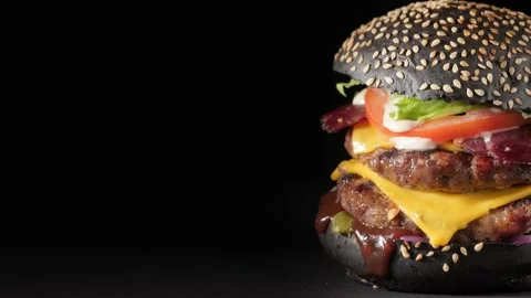 Black burger with double beef cutlet rotates, close-up, copy space. Video stock 146765730
