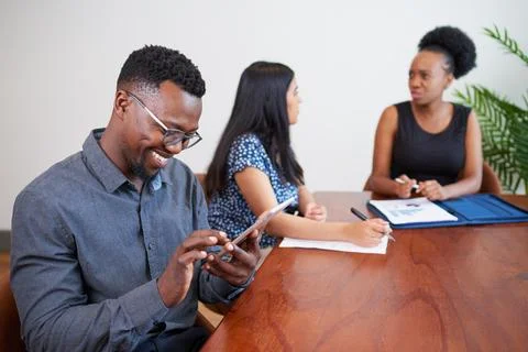Black businessman smiles while using digital tablet at conference table meeting Stock Photos