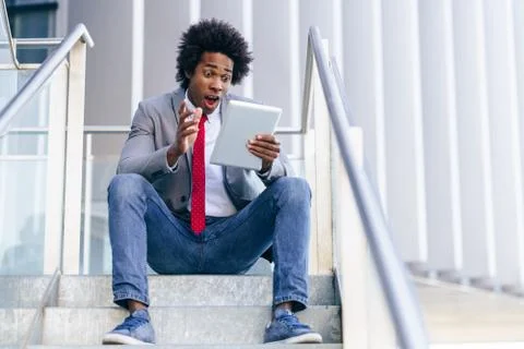 Black Businessman using a digital tablet sitting near an office building. Stock Photos