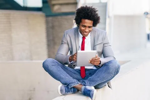 Black Businessman using a digital tablet sitting near an office building. Fotos de archivo