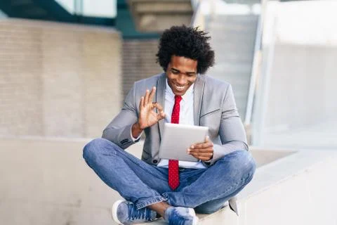 Black Businessman using a digital tablet sitting near an office building. Stock Photos
