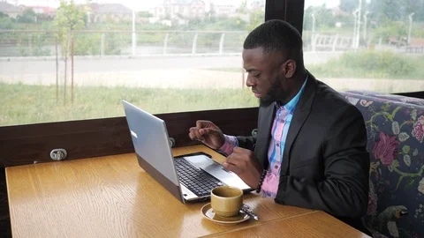 Black businessman is working typing a message on laptop sitting in summer cafe. Video stock 112940375