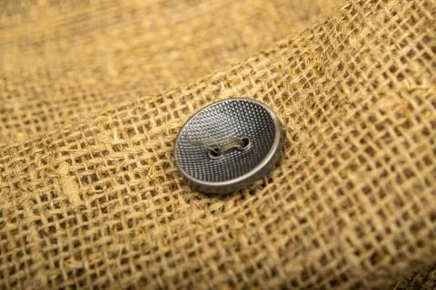 A black button sewn to a piece of burlap. Close up. Stock Photos