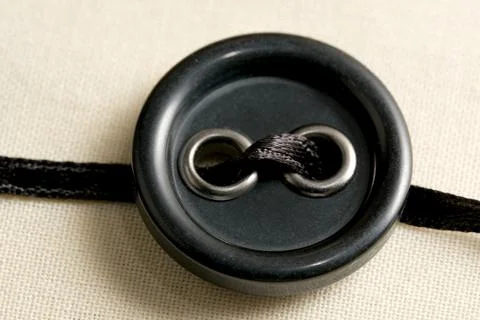 Black button with thread detail resting on a neutral fabric backdrop Stock Photos