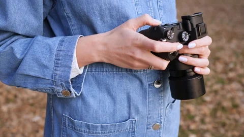 Black camera in female hands, close-up. A woman in denim clothes looks at and Stockbeeldmateriaal 124553872