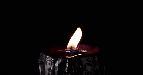 A black candle burning. Isolated candle burning with dark background. Black Stock Footage 159219558