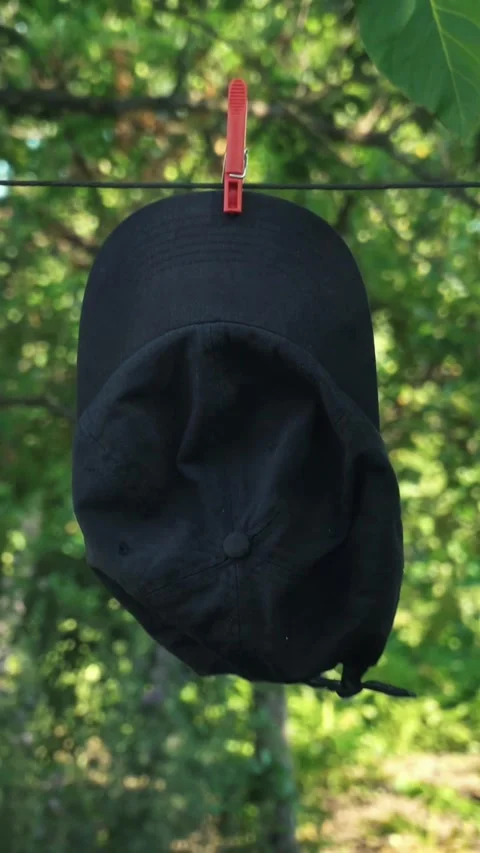 Black cap hanging on a clothesline with a bright green background, showcasing Stock Footage 338306665