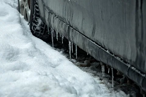 A black car covered with a layer of mud and frozen icicles on the threshold. Stock Photos