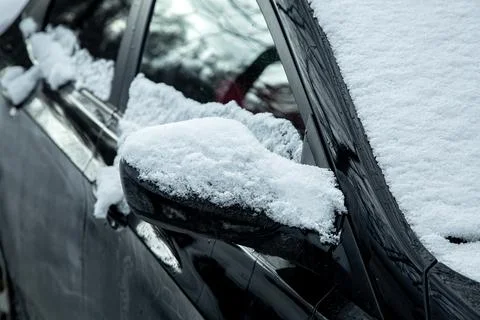 Black car covered with a layer of snow, rear-view mirror close-up. Stock Photos
