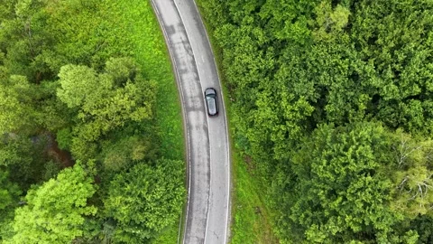 Black car driving along winding rural road surrounded by lush greenery. Vidéo 340169848