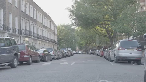Black car driving down residential street lined with parked vehicles Stock Footage 342564672