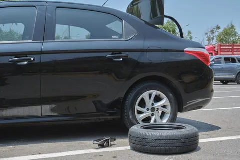 Black car with flat tire replacing it on roadside Stockfoto's